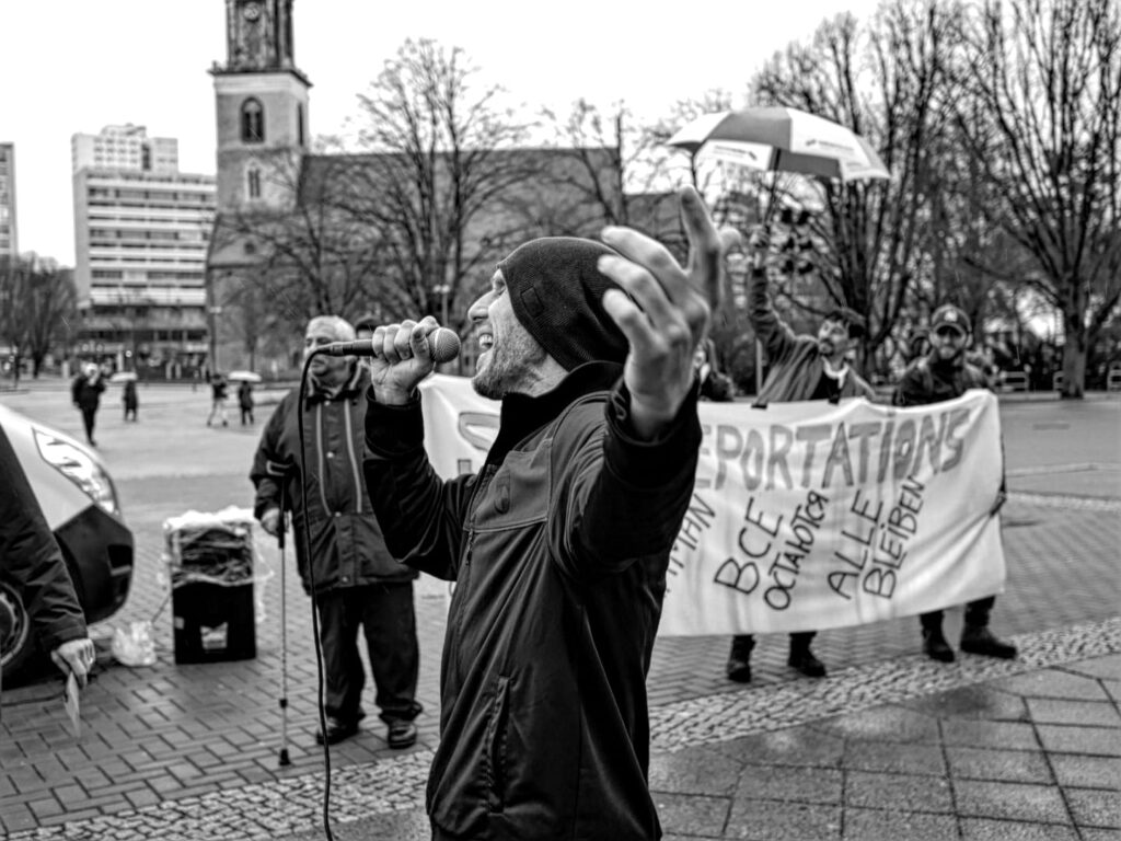 Foto von der Berlin Demonstration gegen die Abschiebung von Roma* nach Moldau. Im Vordergrund der Musiker Mal Élevé, der vor der Protestgruppe performt.