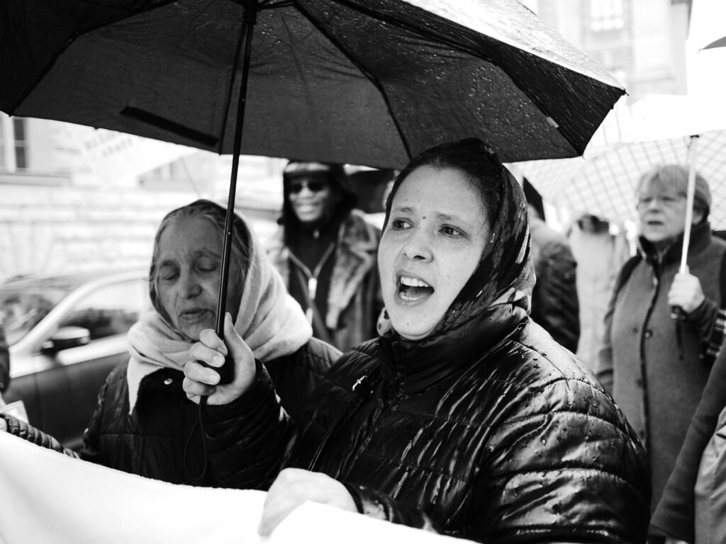 Foto von der Berlin Demonstration gegen die Abschiebung von Roma* nach Moldau. Schwarz-weiß Aufnahme zweier demonstrierenden weiblich gelesenen Personen mit Schirm.