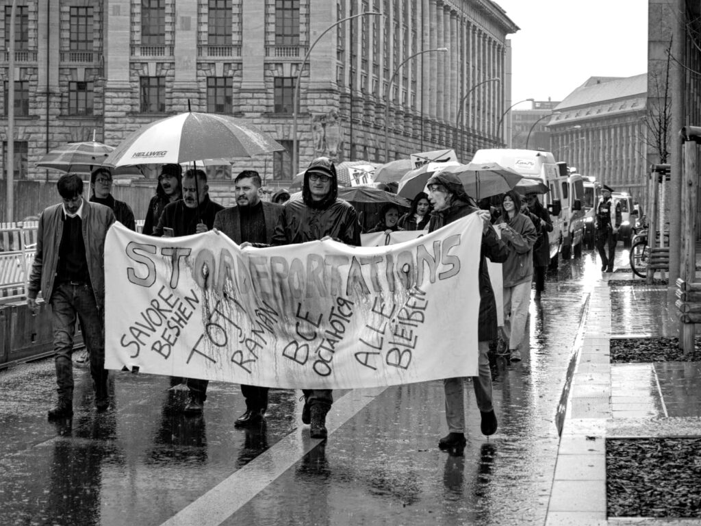 Foto von der Berlin Demonstration gegen die Abschiebung von Roma* nach Moldau. Menschen halten ein Transparent mit der Aufschrift „Stop Deportations“.