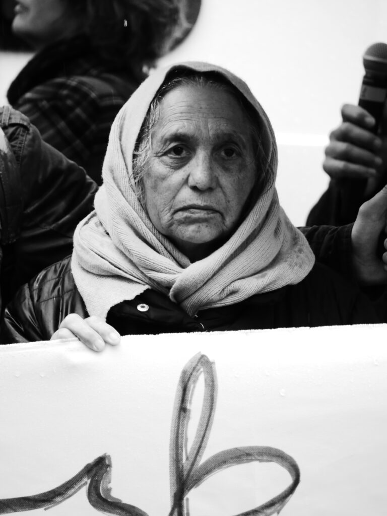 Foto von der Berlin Demonstration gegen die Abschiebung von Roma* nach Moldau. Schwarz-weiß Porträtaufnahme einer weiblich gelesenen Person in einer Menschenmenge.
