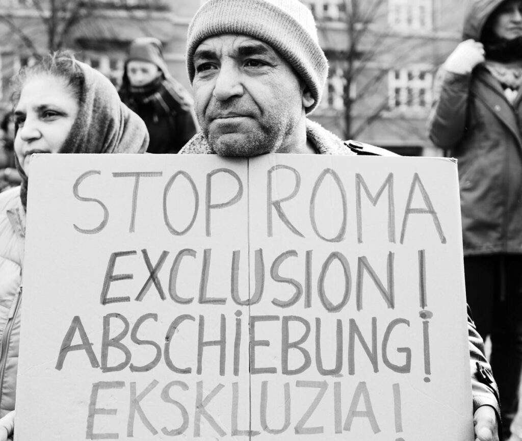 Beitragsbild zur Kritik am Koalitionsvertrag des Bare-Bündnis Berlin. Zu sehen ist eine Person. Sie hält ein Demoschild. Auf dem steht: "Stop Roma Abschiebung". 